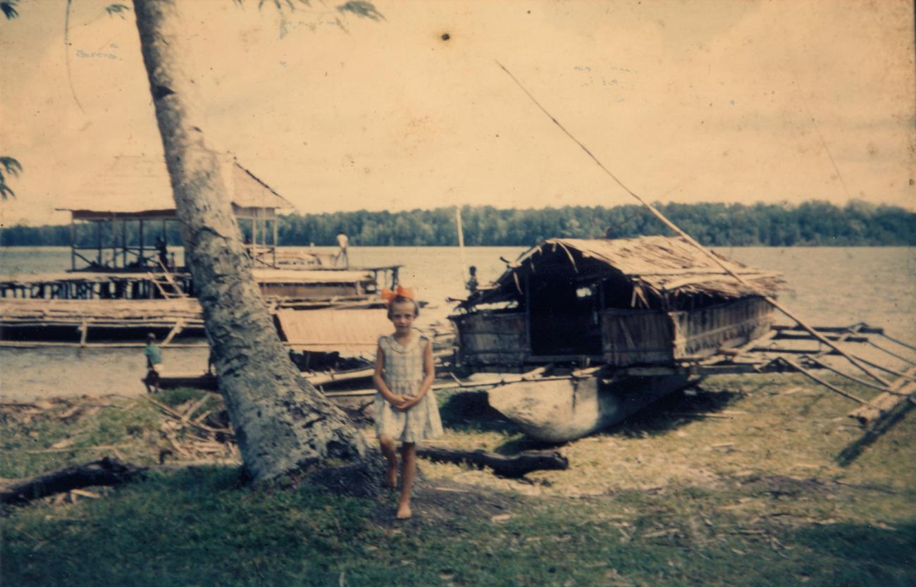 BD/309/35 -
Dorp Konda, westers meisje met op achtergrond vlerkprauw op de kant en baai