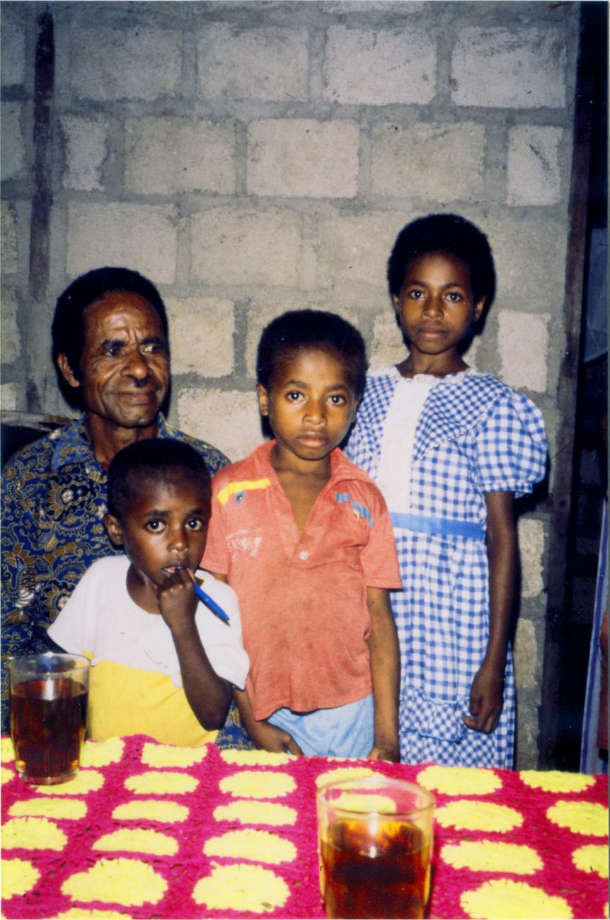 BD/309/72 -
Dorp Teminabuan, man met kinderen bij tafel met limonade
