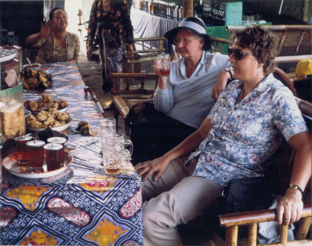 BD/309/76 -
Dorp Bogor, westerse jonge en wat oudere vrouw aan de maaltijd. Niet plaatsen, niet in Nieuw Guinea