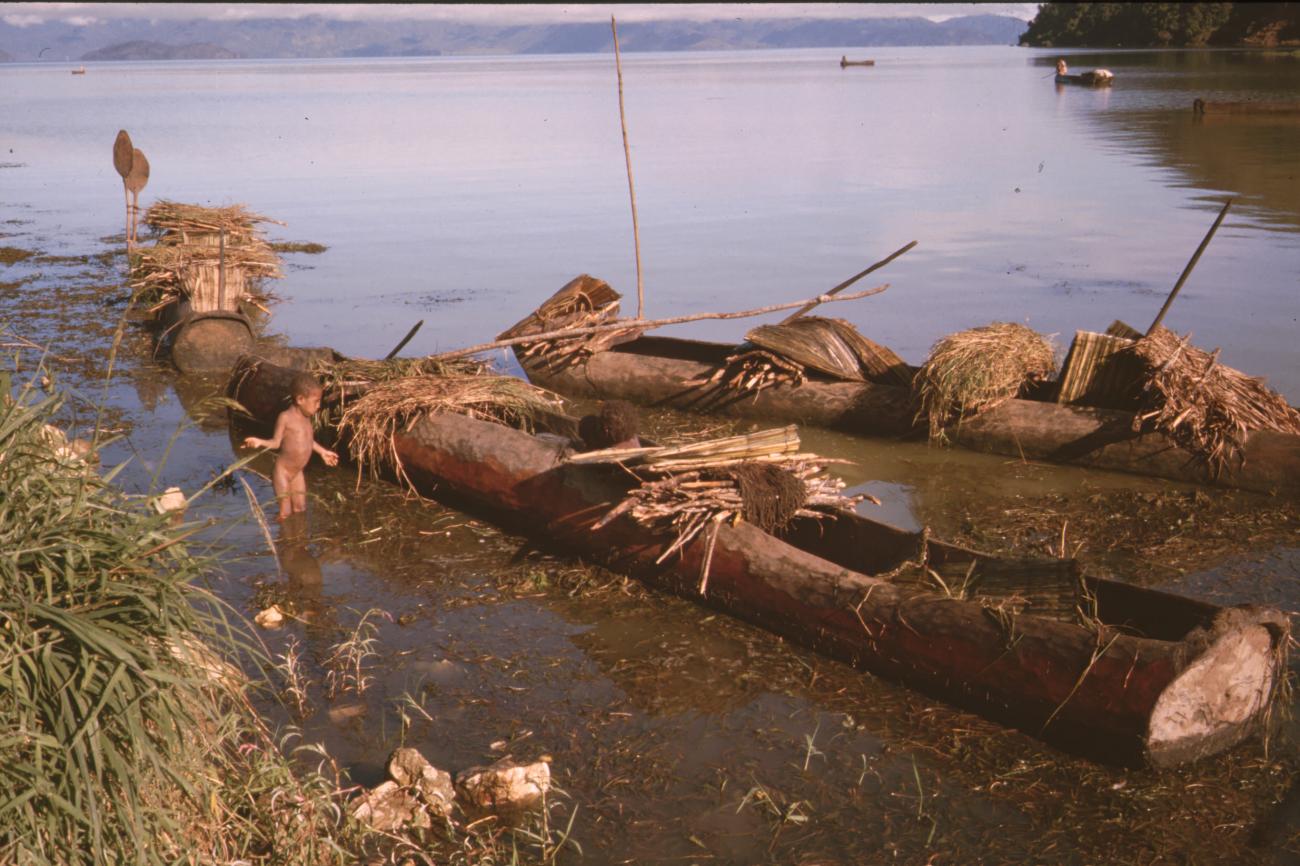 BD/132/170 - 
jongen naast drie prauwen met houttrossen in water
