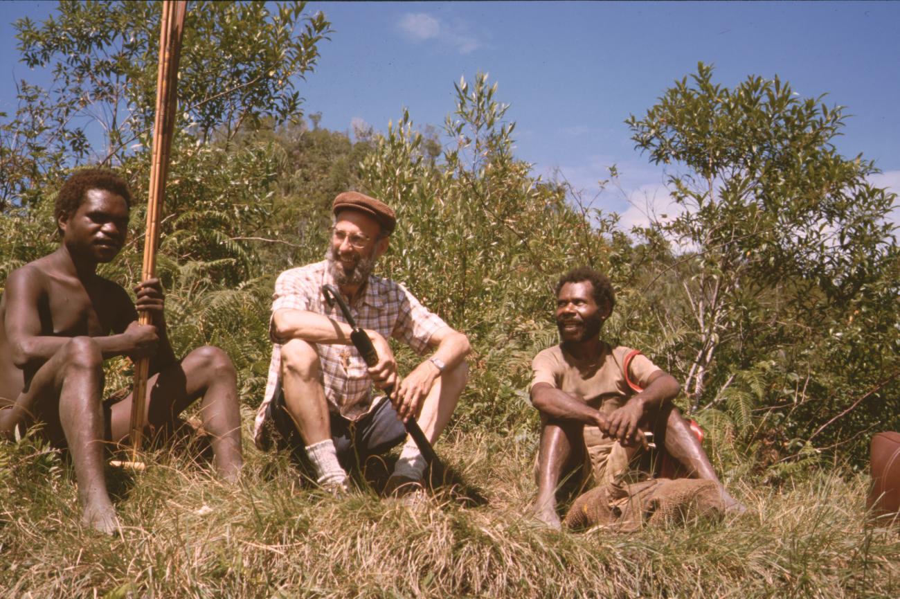 BD/132/172 - 
pater Andringa met paraplu tussen twee Papua&#039;s
