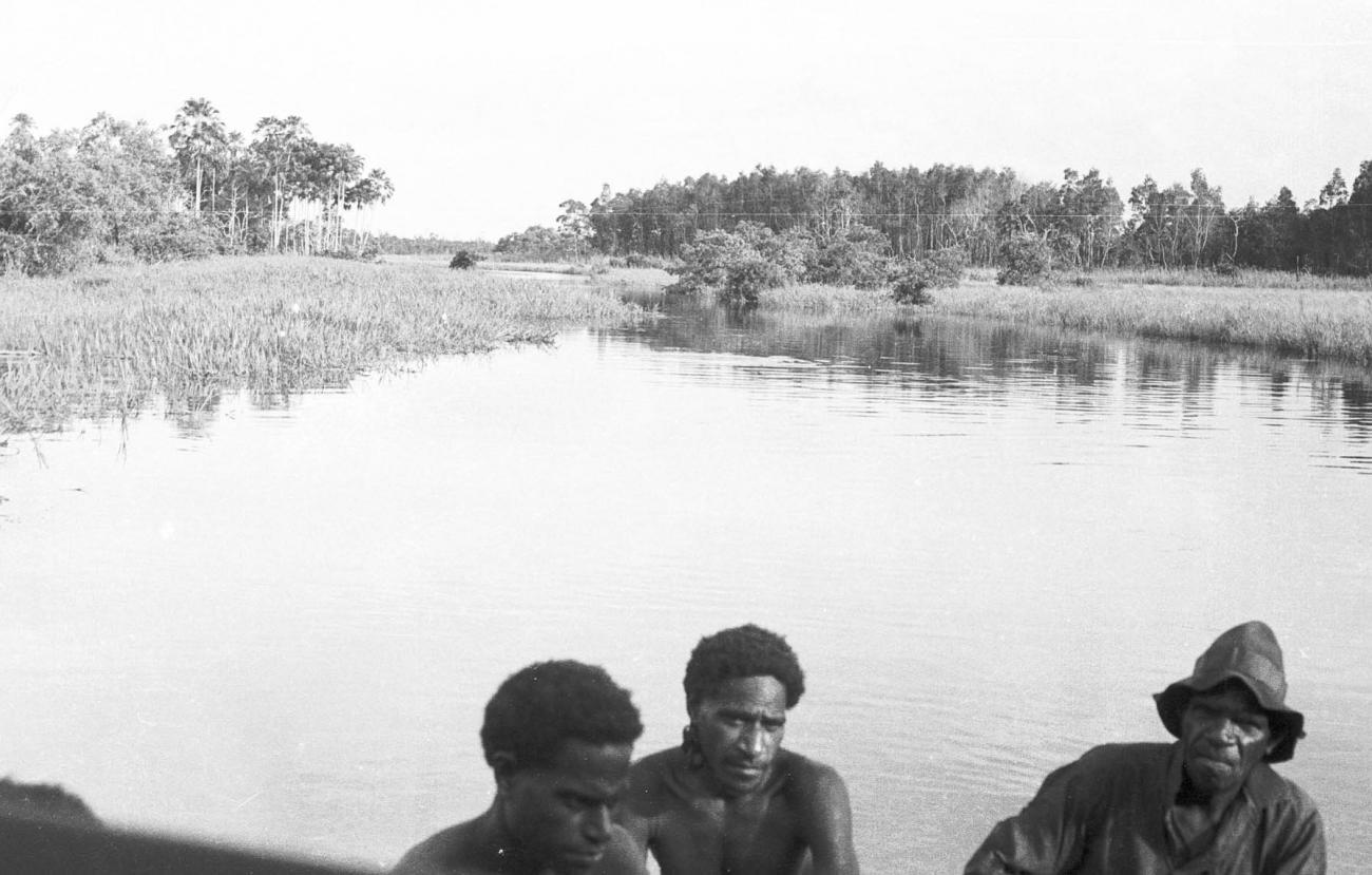 BD/133/322 -
Tocht Merauke-Kepi-Cook: Uitzicht over het water en riet met Papoea's op de voorgrond