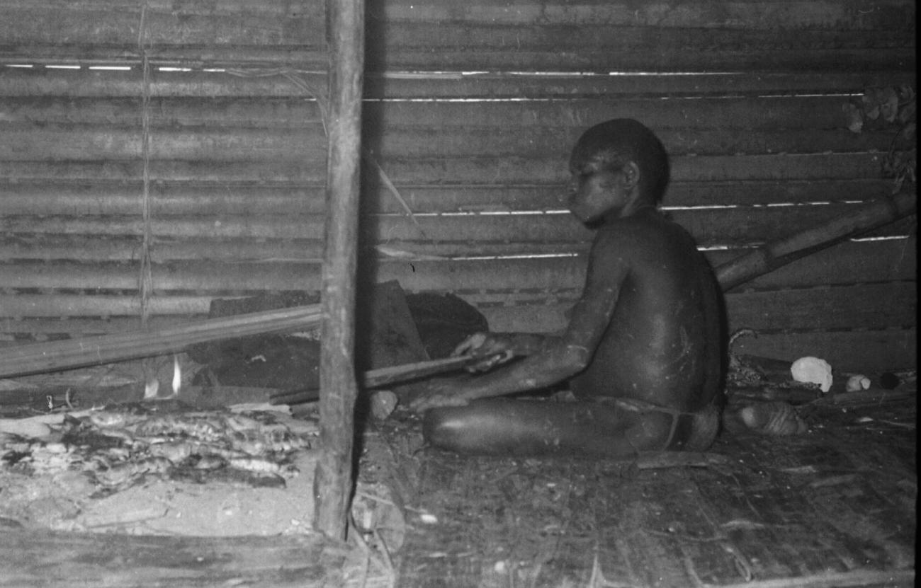 BD/133/62 -
Trip Merauke-Kapi: Marind-anim man sitting near the fire place