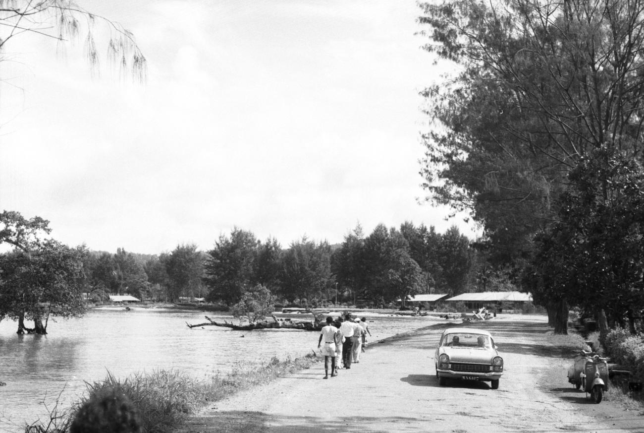BD/133/900 -
Straatbeeld van weg langs rivier, met mensen en auto