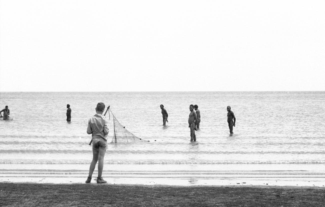 BD/133/983 -
Groep Papoea's zet een visnet uit in het water, met op de voorgrond een westerse jongen