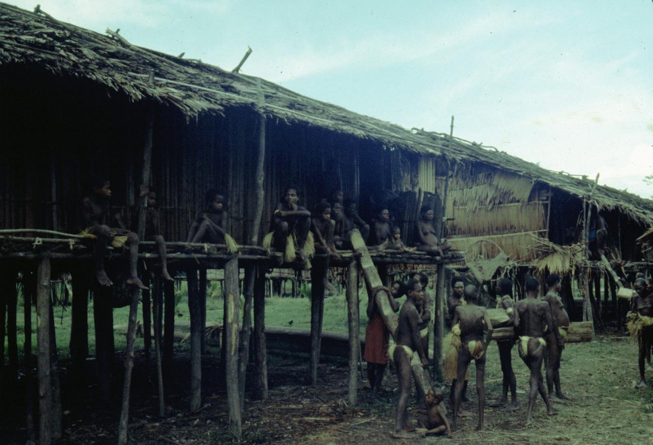 BD/216/353 - 
Paalwoning in het dorp met vrouwen en kinderen op de waranda en voor het huis
