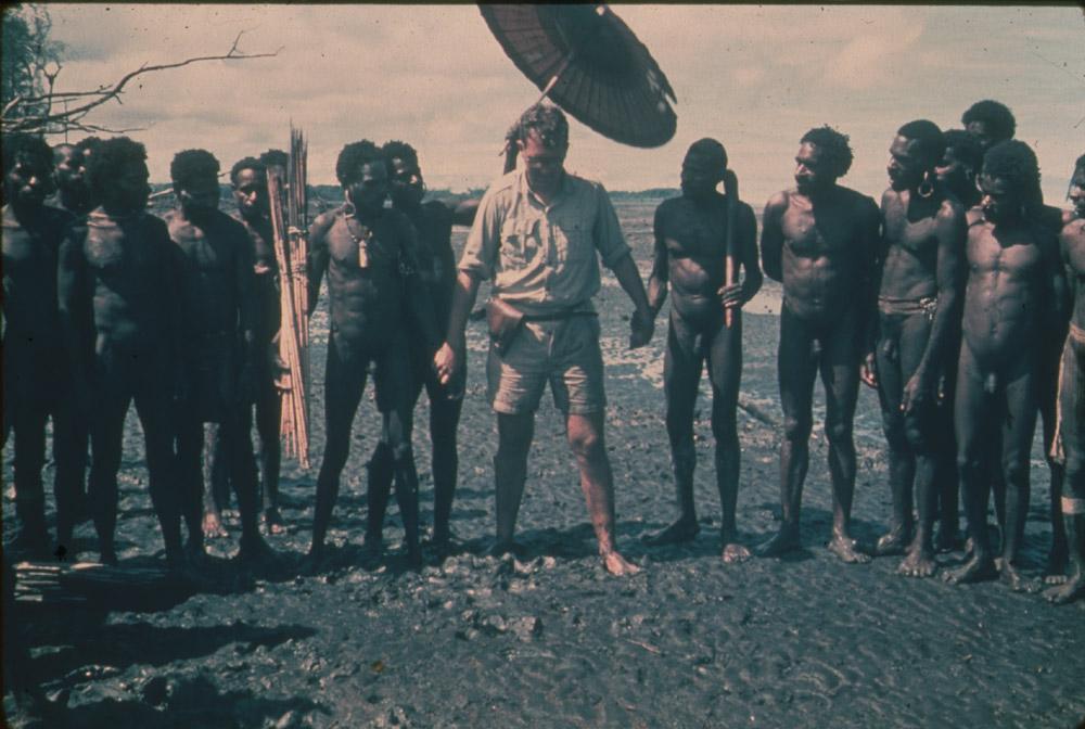 BD/30/99 -
Administration officer under an umbrella on a muddy beach with Asmat men