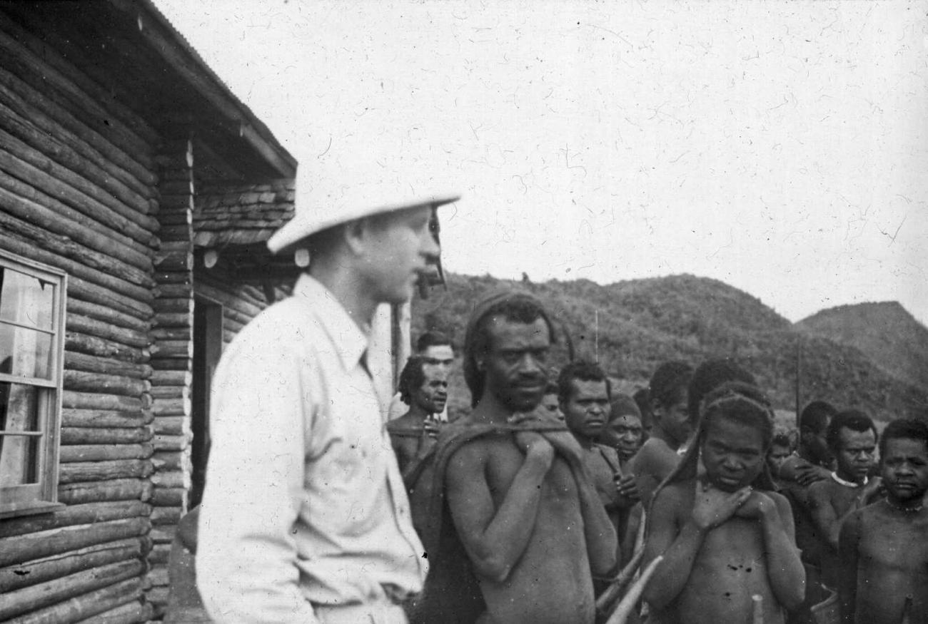BD/66/454 -
De Amerikaanse CAMA-zendeling K.E. Troutman samen met een groep Ekari's voor zijn blokhut bij Enarotali, Wisselmeren