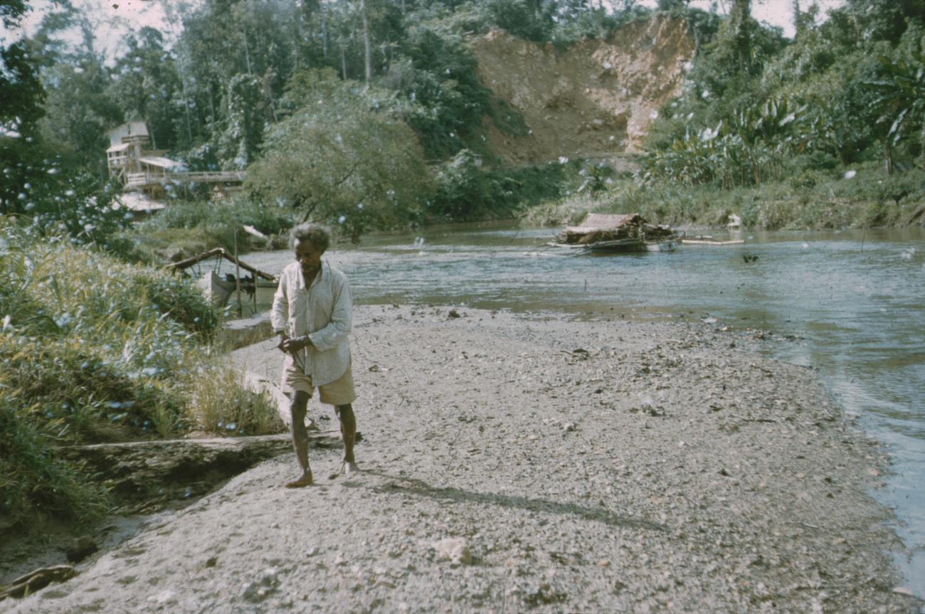 BD/171/562 -
Man bij rivier, op achtergrond prauwen.