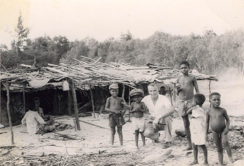 BD/269/1124 -
Franciscaner broeder Henk Blom met Papoea's voor een hut in Kokonau
