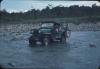 BD/171/275 Een jeep rijdt door stromende rivier bezaaid met kiezelstenen en keien