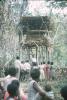 BD/171/98 Onder een hoge houten hut luisteren een groep toeschouwers l